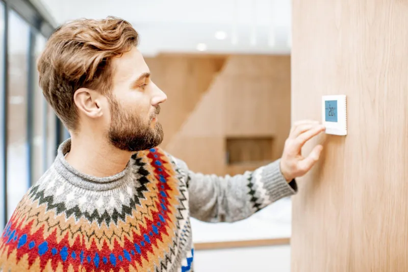 man adjusting programmable thermostat in home - Peter Levi